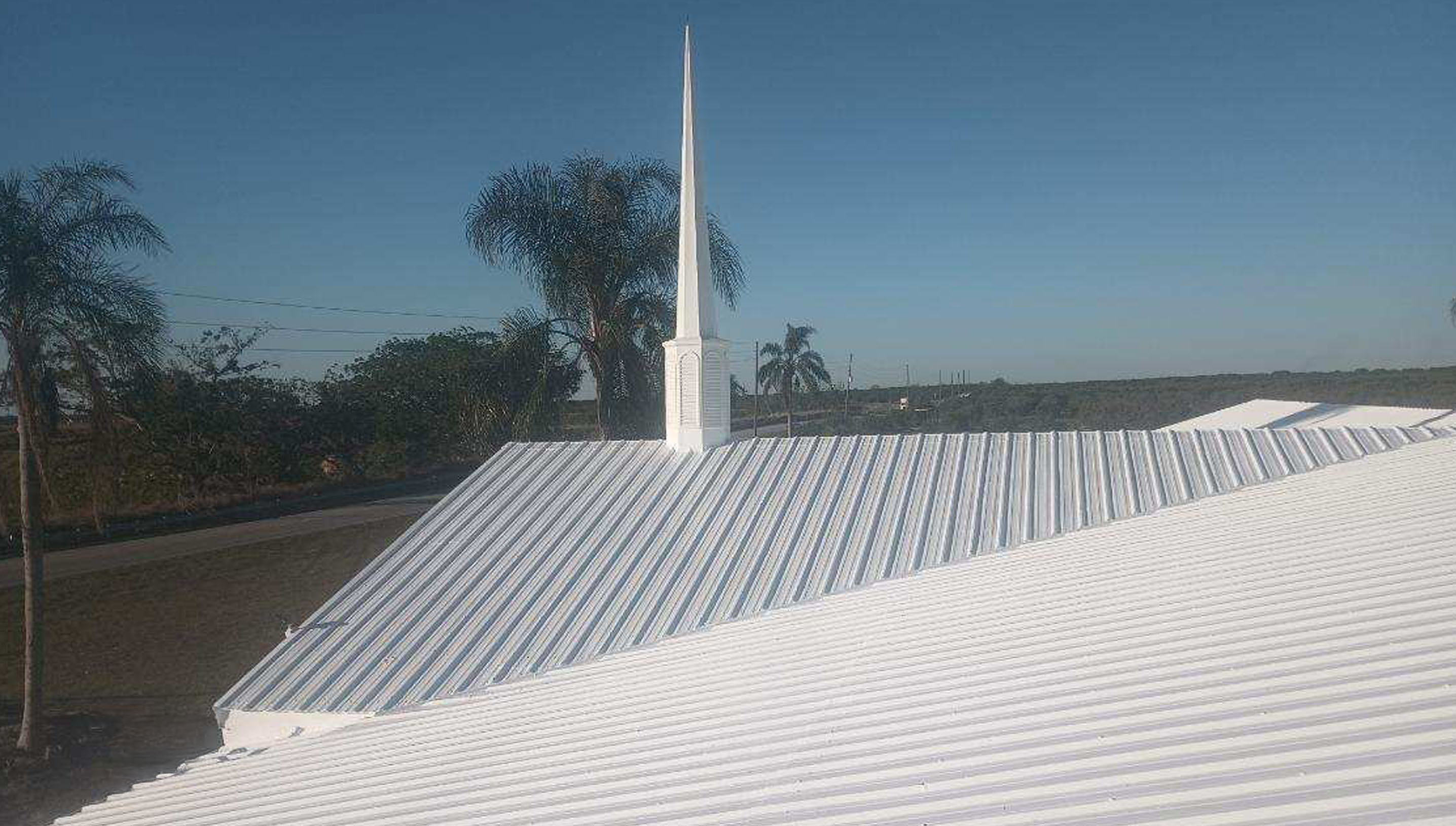 Un tejado de iglesia de metal blanco con una alta aguja blanca contra un cielo azul claro.