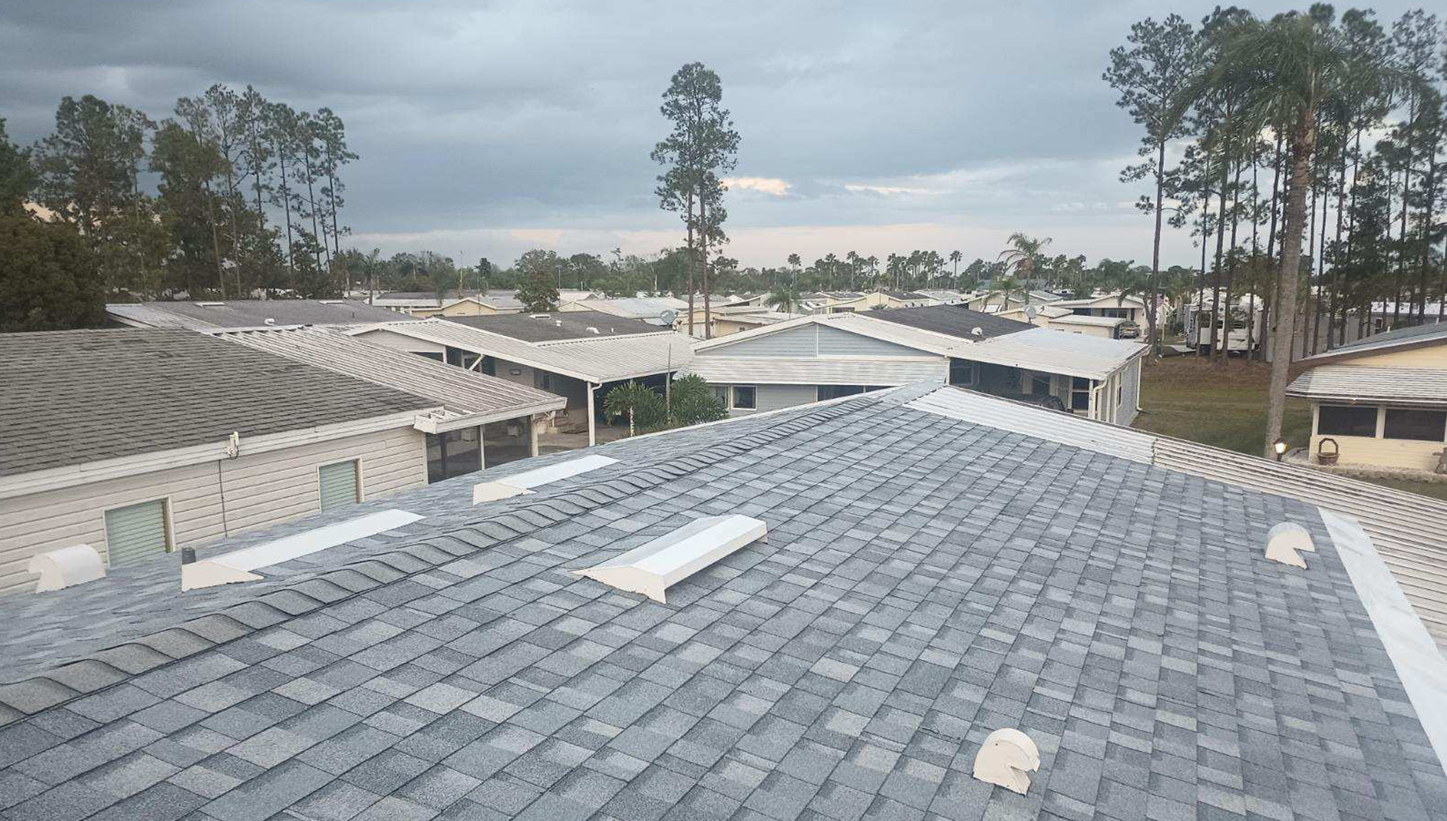 A gray shingle roof with white roof vents under an overcast sky.