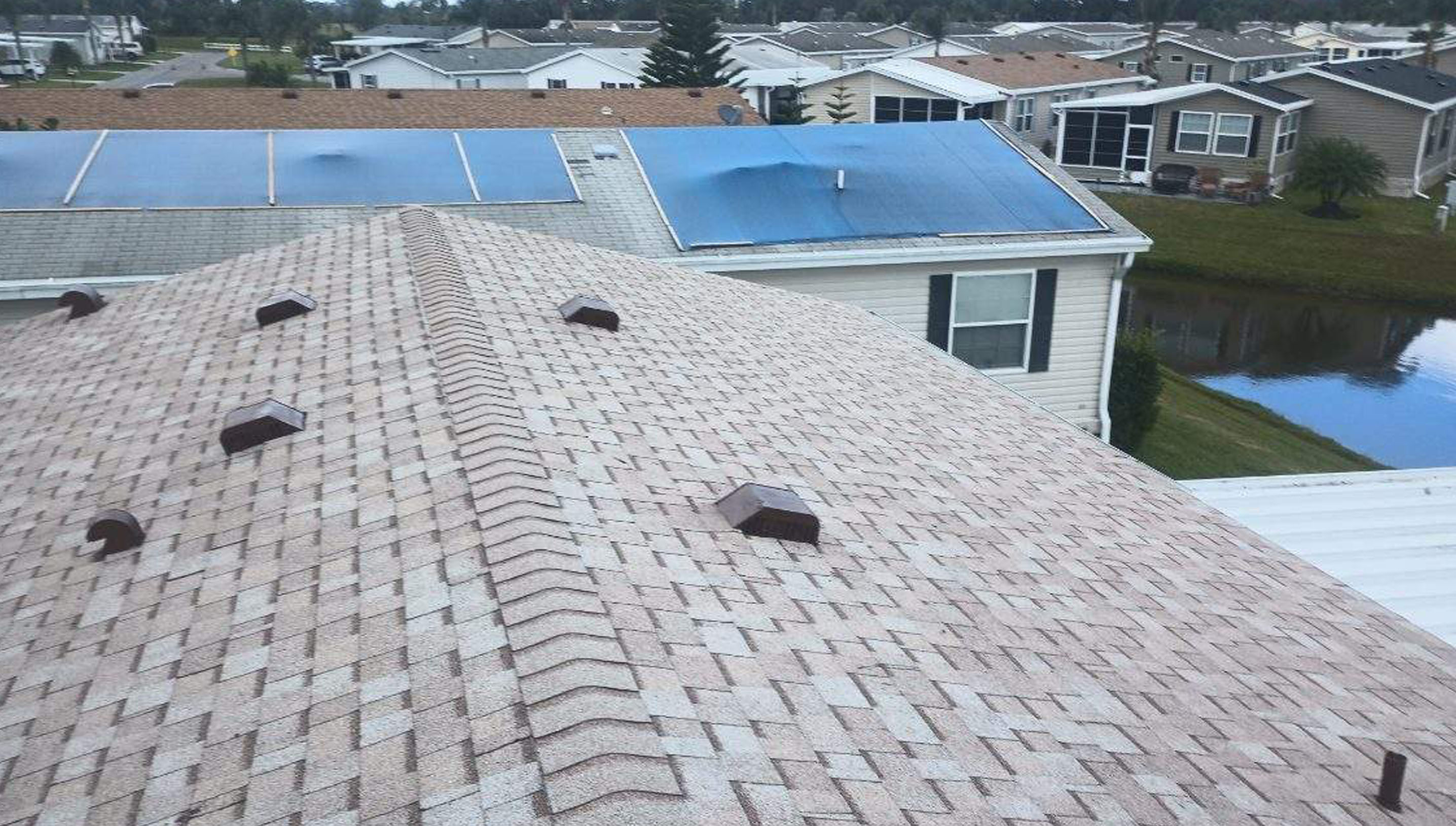 A view of a light brown shingled roof with dark brown roof vents surrounded by residential homes.