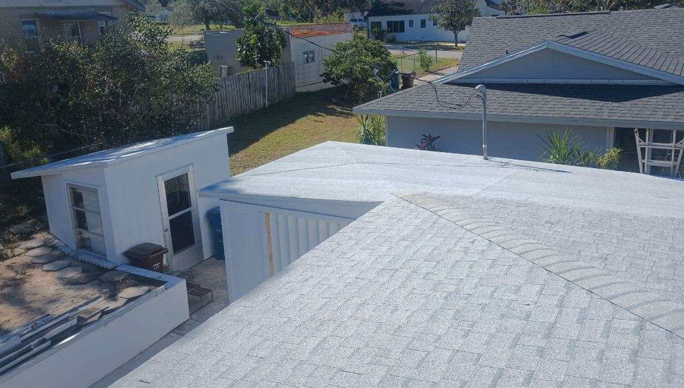 An aerial view of a backyard from a light gray shingled roof surrounded by trees.